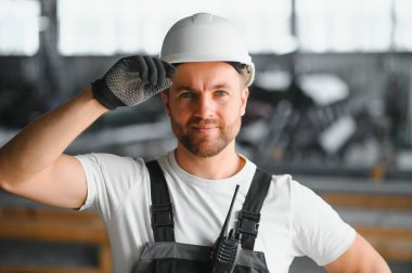 Büyük bir metal fabrikasında kasketli genç bir işçinin portresi. Shiftman bitmiş ürünlerin deposunda..