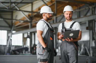 Hard Hats 'ta İki Ağır Sanayi Çalışanı Fabrika' da İş Bulma Görevlerini Tartışıyor, Laptop Bilgisayarını Kullanıyor.