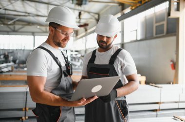 Hard Hats 'ta İki Ağır Sanayi Çalışanı Fabrika' da İş Bulma Görevlerini Tartışıyor, Laptop Bilgisayarını Kullanıyor.