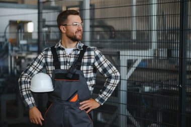 Gülümseyen ve mutlu çalışan. Fabrikadaki endüstriyel işçilerin portresi. Beyaz şapkalı genç teknisyen..