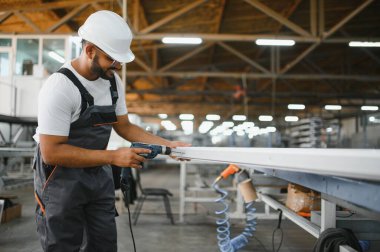 Özel üniformalı mutlu Hintli erkek fabrika işçisi ve metal pencere ve kapılarda alüminyum çerçeve tutan beyaz başlıklı adam..