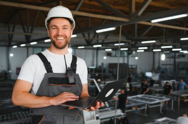 Gülümseyen ve mutlu çalışan. Fabrikadaki endüstriyel işçilerin portresi. Beyaz şapkalı genç teknisyen..