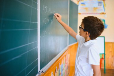 Sevimli küçük okul çocuğunun fotoğrafı tebeşir yaz matematik problemini çöz şık üniformalı sınıf karatahta arka planı