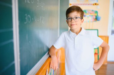 Sevimli küçük okul çocuğunun fotoğrafı tebeşir yaz matematik problemini çöz şık üniformalı sınıf karatahta arka planı