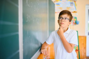 Sevimli küçük okul çocuğunun fotoğrafı tebeşir yaz matematik problemini çöz şık üniformalı sınıf karatahta arka planı