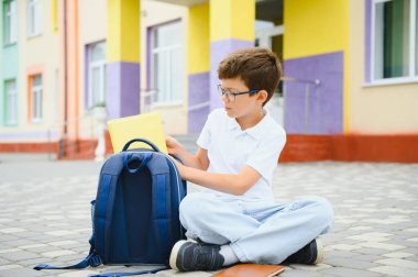 Portrait of a junior high school student sitting and reading a book near the school. Learning concept. clipart