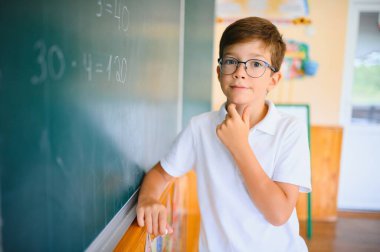 Sınıftaki yeşil okul yönetim kurulunun yanındaki komik öğrenci. İlkokul. Okula geri dön..