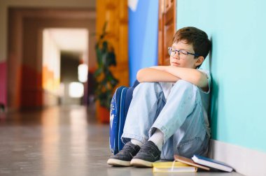 Genç çocuk okulda üzgün bir şekilde yalnız oturuyor. Kopya alanı ile zorbalık, ayrımcılık ve ırkçılık kavramı.