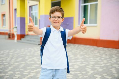 Okulun yanında duran küçük çocuk portresi. Okul başlamadan önce okulun kapısında neşeli bir çocuk. Okula geri dön..