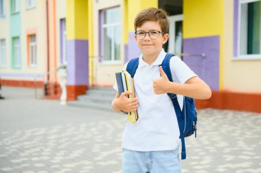 Okulun yanında duran küçük çocuk portresi. Okul başlamadan önce okulun kapısında neşeli bir çocuk. Okula geri dön..