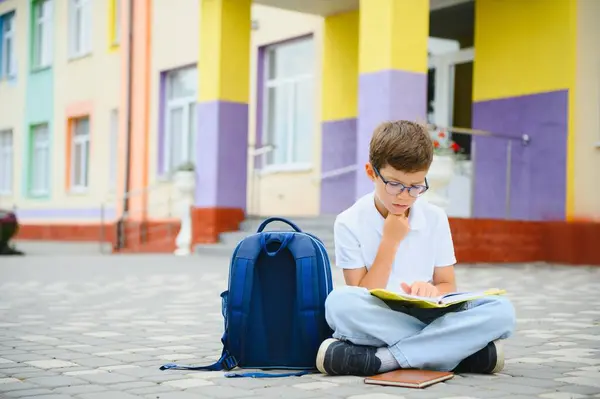 stock image Schoolboy with backpack and books sitting. Beginning of lessons. First class. Back to school concept. Pupil with books and backpack outside school. Education.