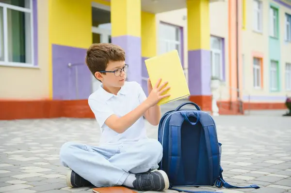 stock image Portrait of a junior high school student sitting and reading a book near the school. Learning concept.