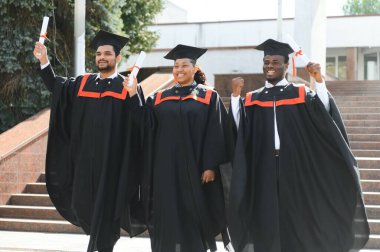 Eğitim, mezuniyet ve halk konsepti. Havan topu ve diplomalı bekarlık elbisesi giyen bir grup mutlu uluslararası öğrenci..