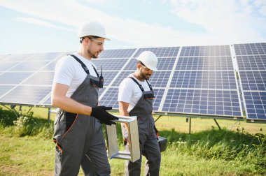 Gri üniforma giyen iki yetenekli işçi veya zanaatkar, teknisyenler temiz enerji ve elektrik tedariği için güneş panelleri kuruyorlar..