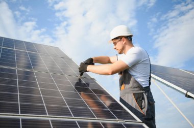 Fotovoltaik güneş modülleri monte eden adam teknisyen. Miğferdeki mühendis dışarıda güneş paneli kuruyor..