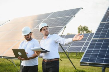 İki mühendis yürüyen ve fotovoltaik panelleri inceleyen güneş enerjisi santrali. Alternatif enerji kavramı ve onun hizmeti.