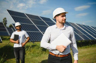 İki mühendis yürüyen ve fotovoltaik panelleri inceleyen güneş enerjisi santrali. Alternatif enerji kavramı ve onun hizmeti.