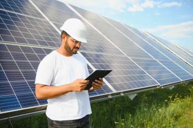 Genç Hintli erkek mühendisin portresi güneş panellerinin yanında duruyor, açık mavi gökyüzü arka planı, yenilenebilir ve temiz enerjisi var. beceri Hindistan, kopyalama alanı.