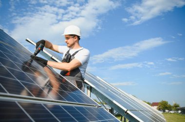 Fotovoltaik güneş modülleri monte eden adam teknisyen. Miğferdeki mühendis dışarıda güneş paneli kuruyor..