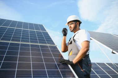 Bir Hintli işçinin portresi, arka plandaki güneş panellerine karşı telsizle konuşuyor..