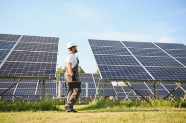 Üniformalı ve aletleri olan Hintli bir işçi güneş paneli çiftliğinde çalışıyor..