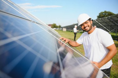Güneş panellerinden oluşan bir alanda çalışan Hintli bir erkek mühendis. Yenilenebilir enerji kavramı.