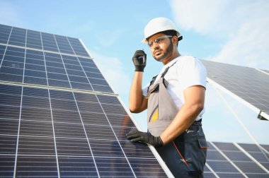 Bir Hintli işçinin portresi, arka plandaki güneş panellerine karşı telsizle konuşuyor..