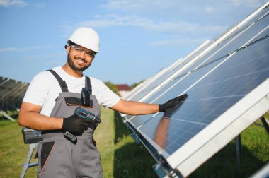 Güneş çiftliğinde üniformalı bir Hintli. Yetkin enerji mühendisi fotovoltaik hücrelerin çalışmalarını kontrol ediyor.