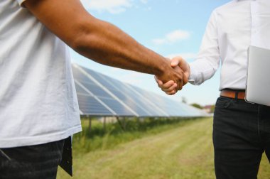 Güneş panelleri arka planında iki erkek mühendis tokalaşması görüntüsü. Yenilenebilir ve yeşil enerji endüstrisi için iş projesi anlaşması ve anlaşması.