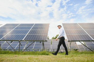 Kırsal kesimde güneşli bir günde beyaz gömlekli bir adam fotovoltaik panellerin yanında duruyor..