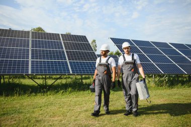 Gri üniforma giyen iki yetenekli işçi veya zanaatkar, teknisyenler temiz enerji ve elektrik tedariği için güneş panelleri kuruyorlar..