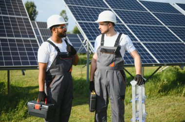 Gri üniforma giyen iki yetenekli işçi veya zanaatkar, teknisyenler temiz enerji ve elektrik tedariği için güneş panelleri kuruyorlar..