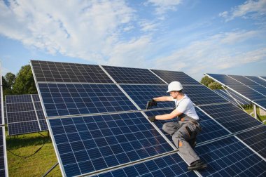 Fotovoltaik güneş modülleri monte eden adam teknisyen. Miğferdeki mühendis dışarıda güneş paneli kuruyor..