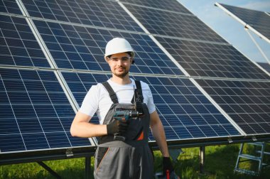 Güneş panelleri üzerinde çalışan üniformalı ve beyaz kasklı bir işçinin portresi..