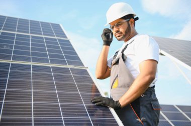 Bir Hintli işçinin portresi, arka plandaki güneş panellerine karşı telsizle konuşuyor..