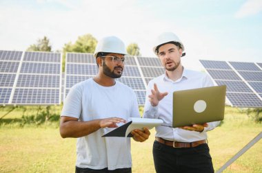 İki mühendis yürüyen ve fotovoltaik panelleri inceleyen güneş enerjisi santrali. Alternatif enerji kavramı ve onun hizmeti.