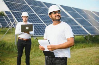 İki mühendis yürüyen ve fotovoltaik panelleri inceleyen güneş enerjisi santrali. Alternatif enerji kavramı ve onun hizmeti.