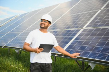 Erkek Arap mühendis güneş panelleri sıraları ile sahada duruyor.