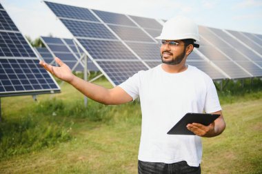 Güneş panellerinden oluşan bir alanda çalışan Hintli bir erkek mühendis. Yenilenebilir enerji kavramı.