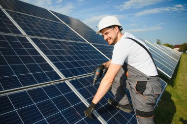 Güneş panelleri üzerinde çalışan üniformalı ve beyaz kasklı bir işçinin portresi..