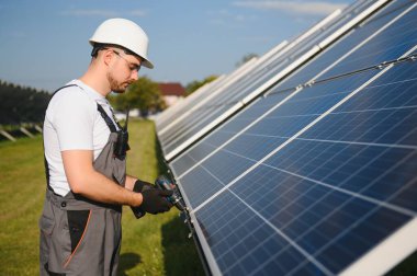 Erkek işçilerin güneş modülleri kurarken ve fotovoltaik güneş dizisini desteklerken yan görünümü. Güneş paneliyle çalışırken kaskını takan bir elektrikçi. Güneş enerjisi kavramı.