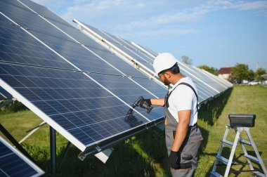 Üniformalı ve aletleri olan Hintli bir işçi güneş paneli çiftliğinde çalışıyor..