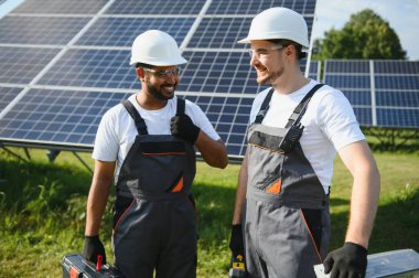 Gri üniforma giyen iki yetenekli işçi veya zanaatkar, teknisyenler temiz enerji ve elektrik tedariği için güneş panelleri kuruyorlar..