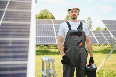Güneş panelleri üzerinde çalışan üniformalı ve beyaz kasklı bir işçinin portresi..