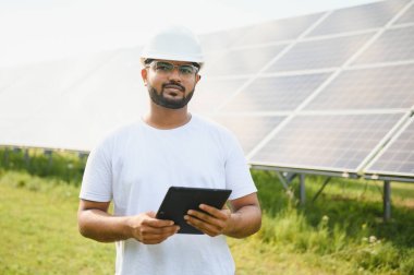 Erkek Arap mühendis güneş panelleri sıraları ile sahada duruyor.