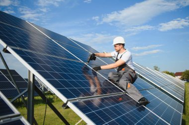 Erkek işçilerin güneş modülleri kurarken ve fotovoltaik güneş dizisini desteklerken yan görünümü. Güneş paneliyle çalışırken kaskını takan bir elektrikçi. Güneş enerjisi kavramı.