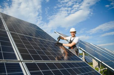 Erkek işçilerin güneş modülleri kurarken ve fotovoltaik güneş dizisini desteklerken yan görünümü. Güneş paneliyle çalışırken kaskını takan bir elektrikçi. Güneş enerjisi kavramı.