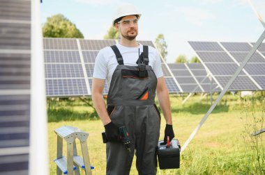 Üniformalı bir işçi portresi ve arka planda güneş panelleri olan beyaz bir kask..