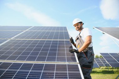 Bir Hintli işçinin portresi, arka plandaki güneş panellerine karşı telsizle konuşuyor..