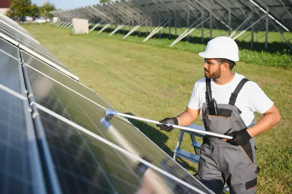 Stock image Professional indian worker cleans solar panels with brush, green electric power technology.